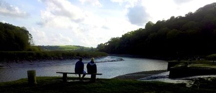 two people on a bench by the river in the evening