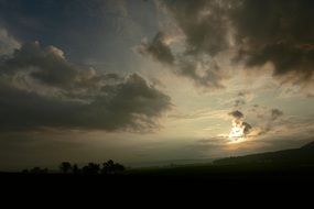 the sun behind the clouds over the hill