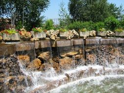 Beautiful artificial waterfall among the green plants and colorful flowers in the park in Erlebnispark
