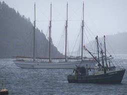 anchored boat and sailing ship in bay at foggy mountains, usa, new england, maine