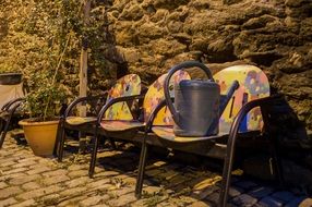 watering can on colorful chairs on the street near the wall
