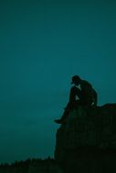 silhouette of man, sitting on rock at night