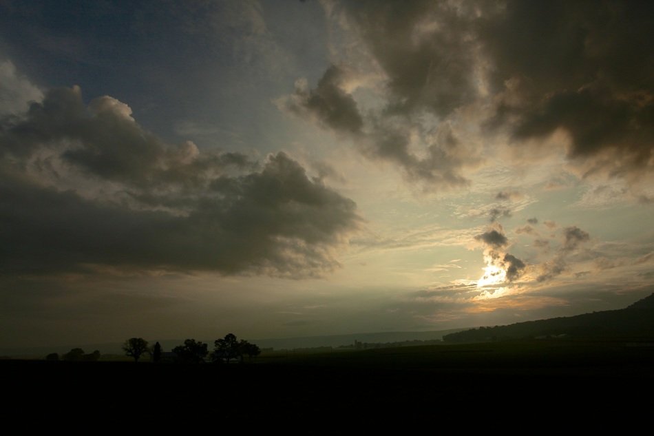 the sun behind the clouds over the hill