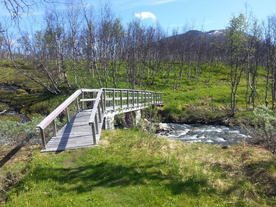 wooden bridge across creek in view of mountain at spring, sweden, norrland