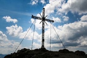 Cross in the Alps on the background of the cloudy sky