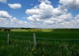 fenced green pasture beneath fluffy clouds