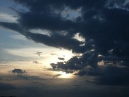 sun behind dark clouds in the sky at dusk