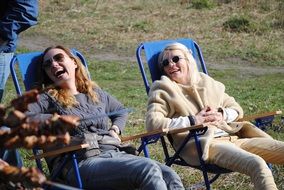 two laughting caucasian girls sitting in armchairs at nature