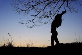 silhouette of a girl with raised arms against the evening sky