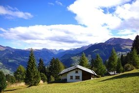 Cute house in green field trees mountain sky view