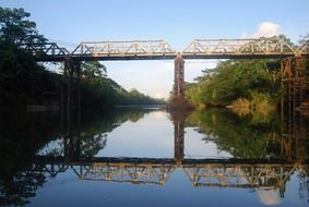 steel bridge across amazon river with reflection on water, ecuador