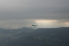 the plane flies over the mountains under dark clouds