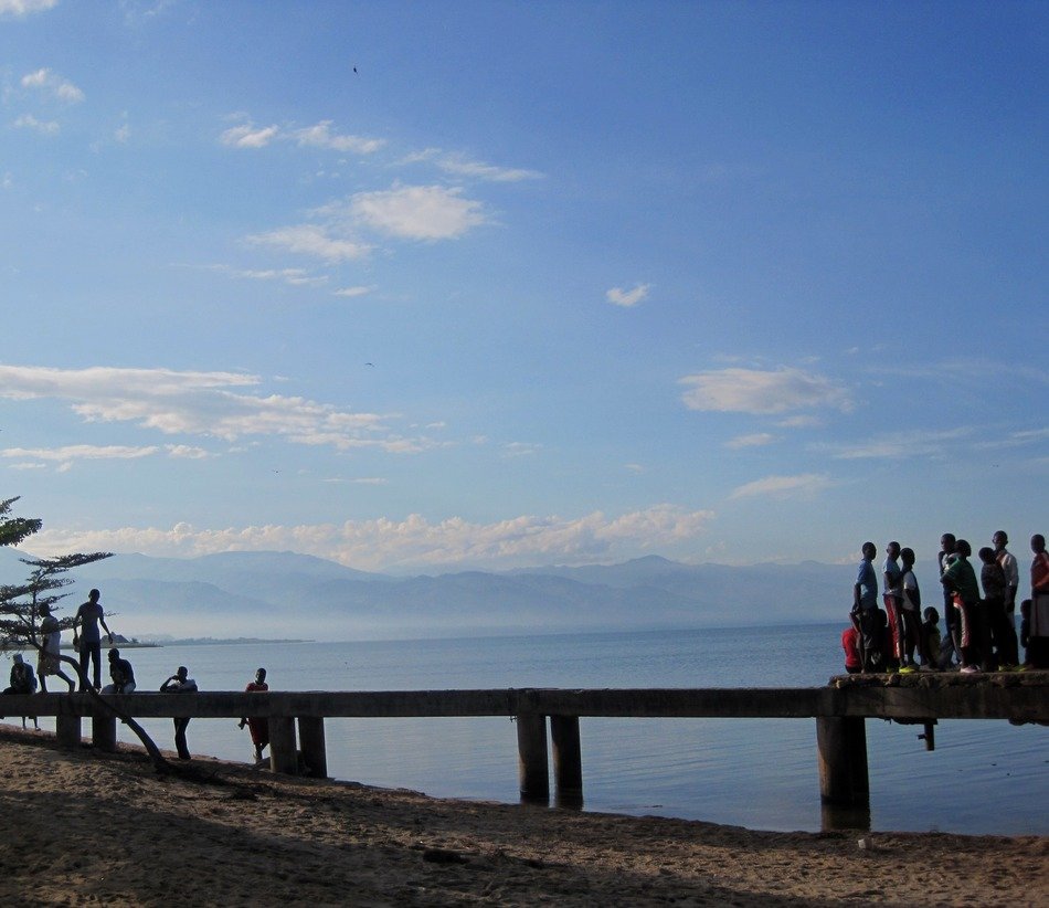 local people on pier at seashore in view of distant mountain range, africa