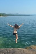girl in a swimsuit jumps into the water from a cliff