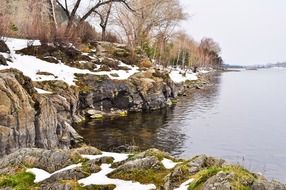 Beautiful rocky shore of a river with colorful plants in the snow