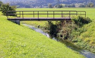 bridge over a small stream among green meadows on the beautiful bright landscape