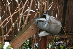 metal watering can hanging on a wooden fence