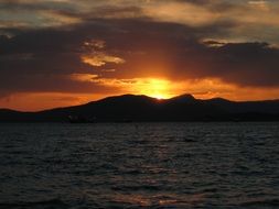 orange sunset in the clouds over the mountains on the sea coast