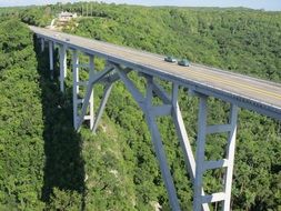 cars on road bridge above forested mountain side, cuba