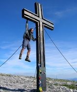 man hanging on big black cross in the mountains