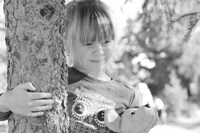 Smiling girl with teddy bear near tree black and white recording