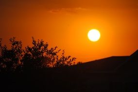 the sun on a bright orange sky above the hill