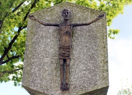 Crucifix on the stone under the green tree near the church