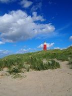 distant red lighthouse on beach under fluffy clouds