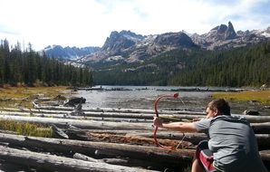 young man shoots a bow on the lake