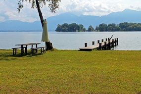 table with benches and pier on lake bank in view of beautiful mountains, germany, chiemsee