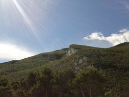sun rays over the top of a green mountain