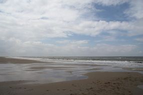 white clouds above wet sand beach