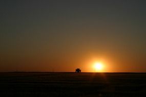 distant view of a tractor on a field in the dark twilight at sunset