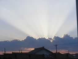 sun beams behind dark cloud at sunset sky