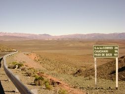 desert landscape with fenced road and roadsign, argentina