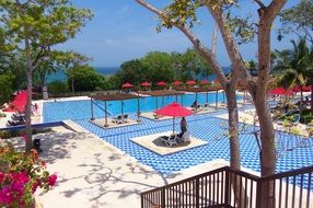 a blue pool and red sun umbrellas at a hotel in Costa Rica