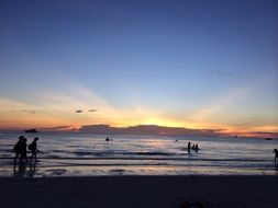 tourists walk along the tropical coast at sunset