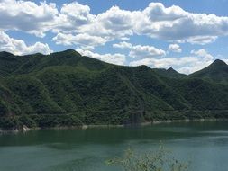 scenic green hills and a lake on the background of sky with white clouds