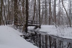 snow landscape of a wooden bridge over a river in the forest