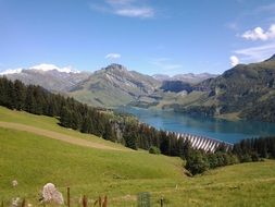 Beautiful landscape of green hills with trees and mountain lake in the background of the Alps