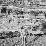 black and white photo of a girl on the beach near the cliff