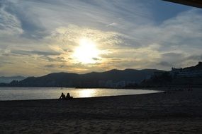 people sit on the beach at sunset