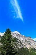 Beautiful mountain peak near the green tree at blue sky with white clouds on background