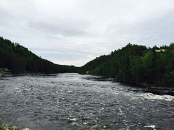 wide river with forested banks at cloudy weather