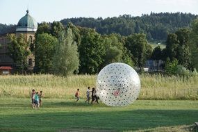 People playing with big baloon on green meadow