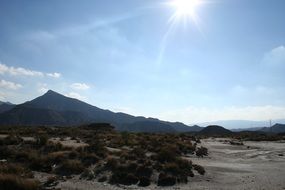 A picturesque desert against the background of volcanic rocks in the glare of the sun