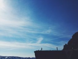 people silhouettes on cliff at blue sky