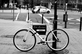 black and white photo of a bicycle near a post on the street