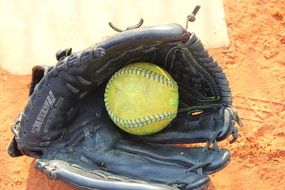 softball ball in leather glove on sand