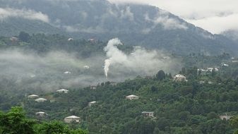 white smoke above village in forest at misty mountains